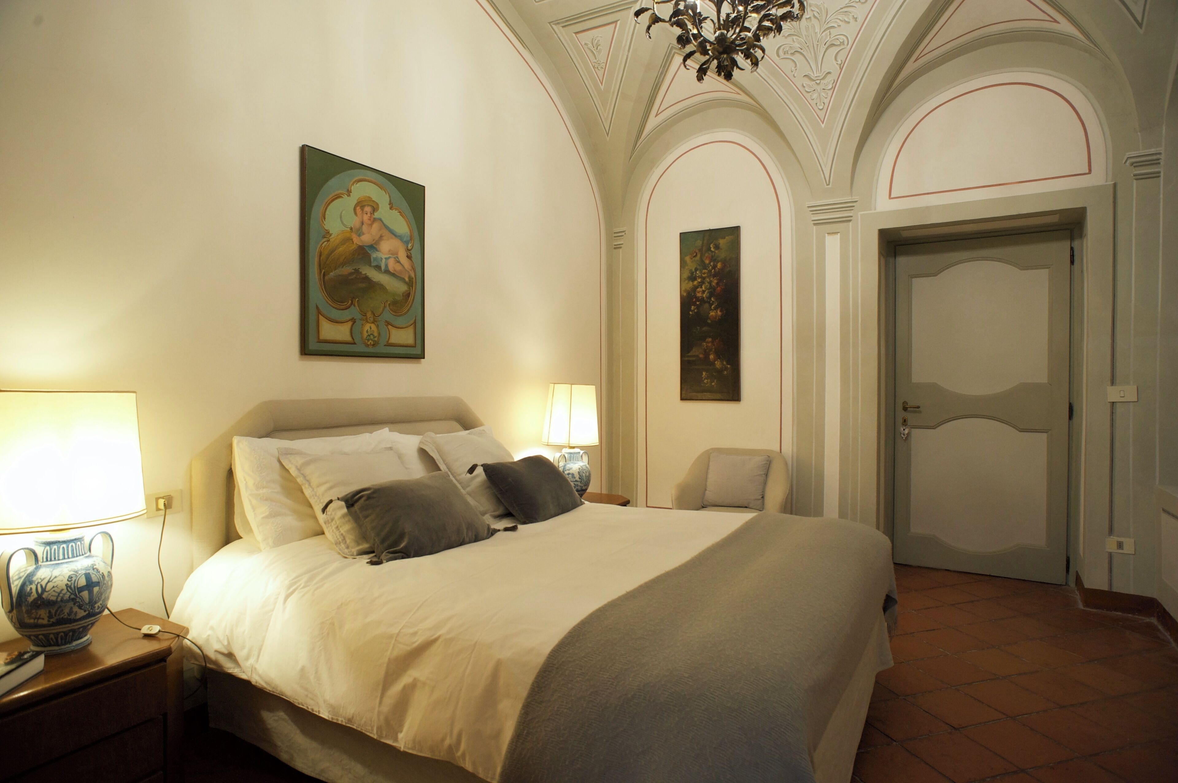 Una habitación de hotel con una cama grande, dos lámparas de noche, un jarrón decorativo y un cuadro en la pared.