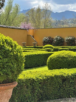 A well-manicured garden with hedges, a stone wall, and a view of distant mountains.