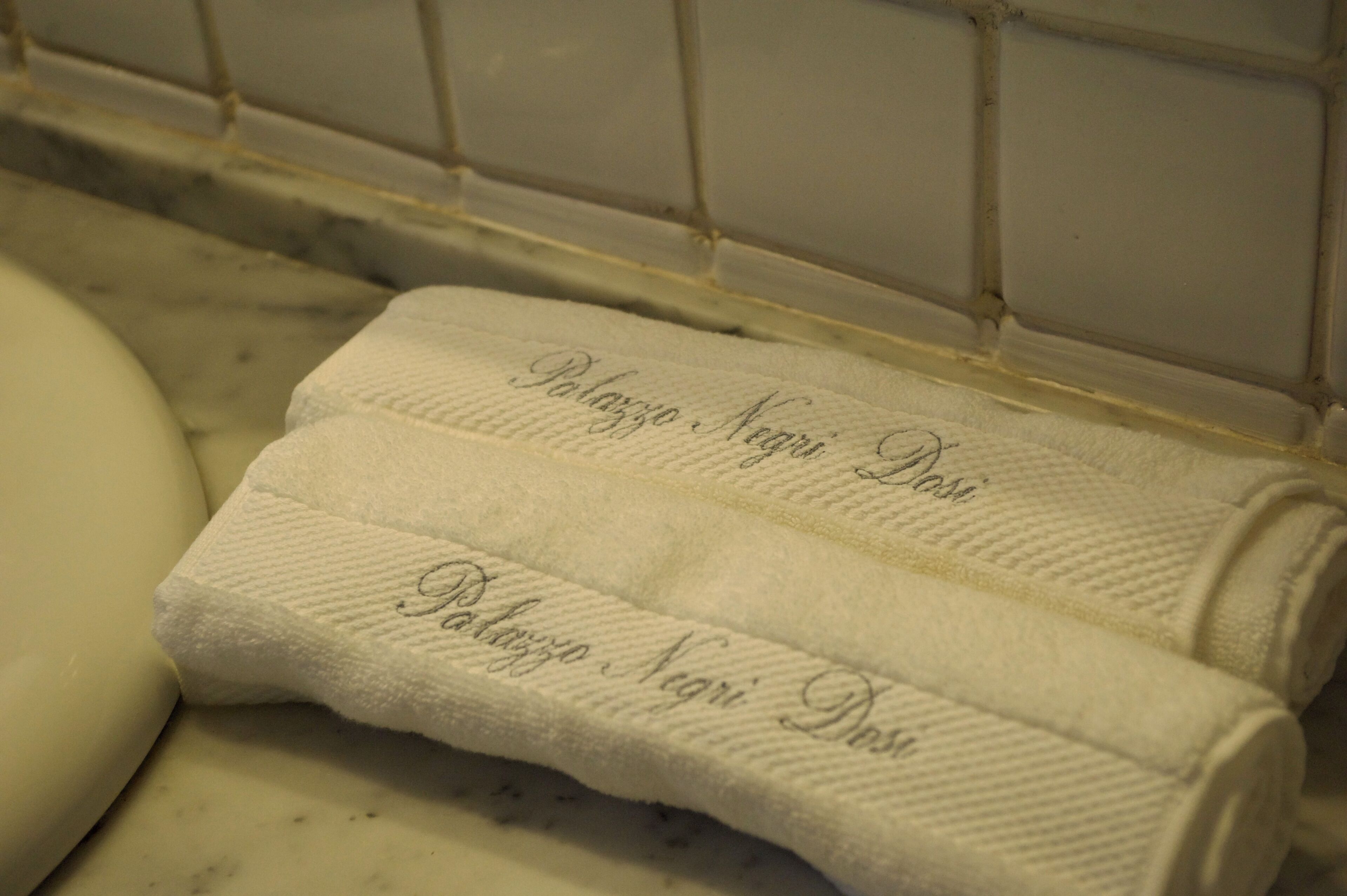 Dues tovellas blanques amb text brodat, damunt d'una superfície blanca, probablement un taulell de bany.