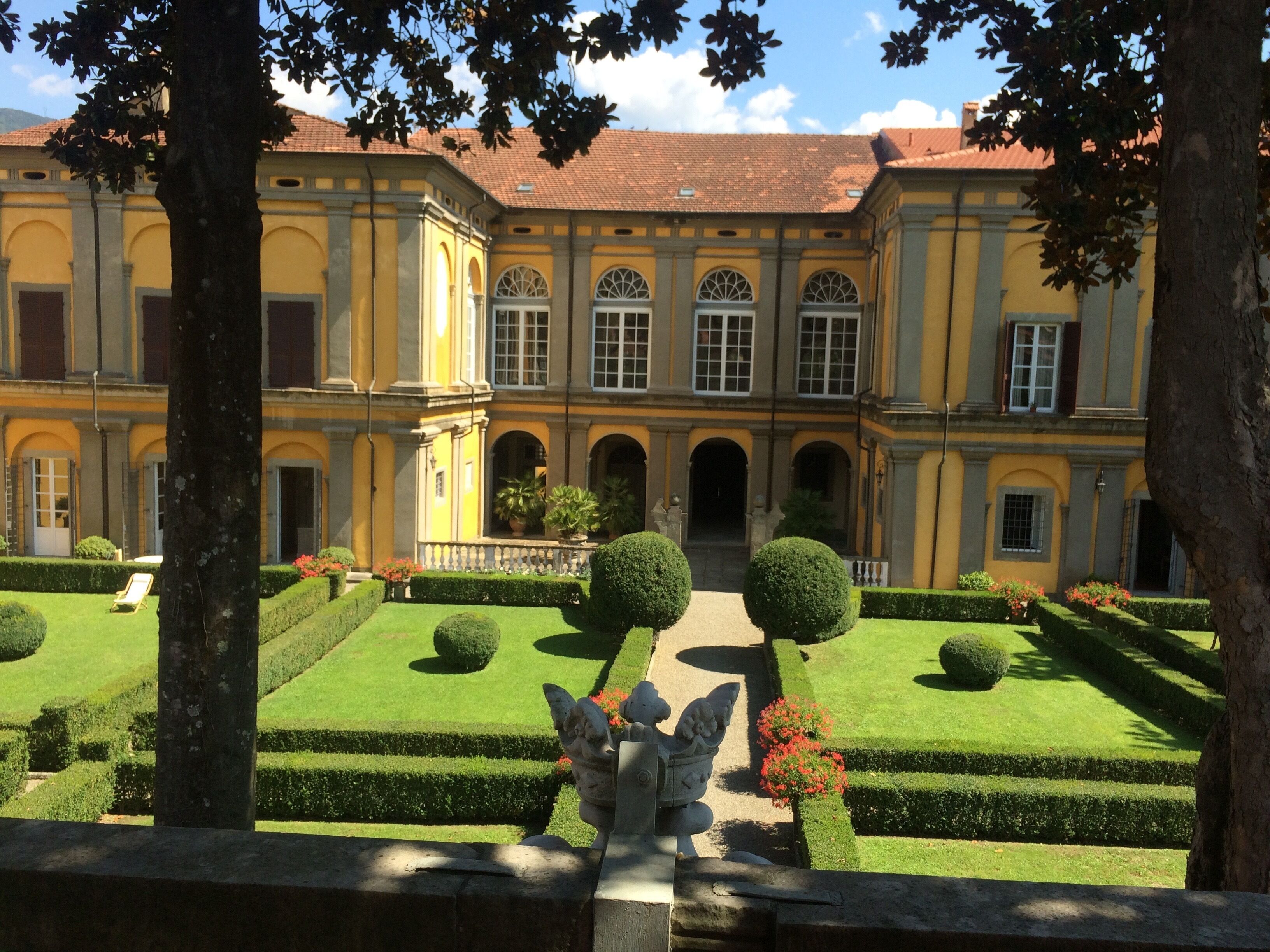 Un patio con una estatua, un edificio con ventanas de arco y un césped bien cuidado.