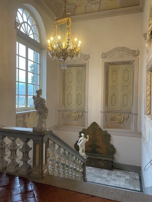 A grand staircase with ornate railings, a chandelier, and decorative moldings.
