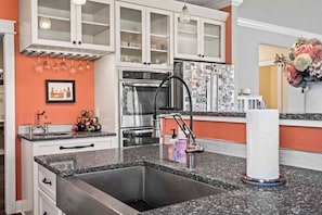 A kitchen with white cabinets, a stainless steel sink, and a refrigerator with magnets. - 6BR Farmhouse Sleeps 14 | Fire Pit + Games + Trail (Traverse City)
