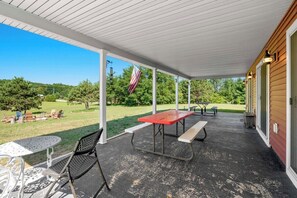 Eine überdachte Terrasse mit Picknicktischen und -stühlen, einer amerikanischen Flagge und Blick auf eine grüne Rasenfläche mit Bäumen.
