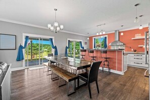 A modern kitchen with a central island, bar stools, and a dining area with a long table and benches. - 6BR Farmhouse Sleeps 14 | Fire Pit + Games + Trail (Traverse City)