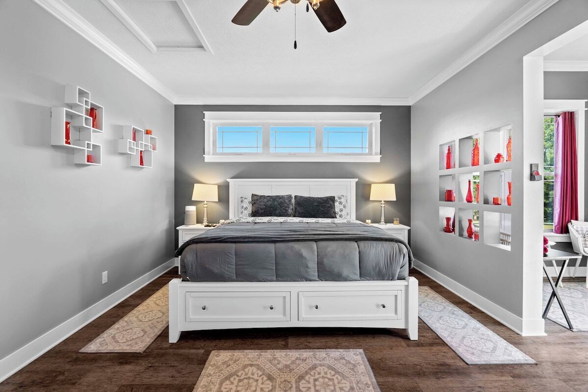 A bedroom with a bed, bedside tables, a ceiling fan, and built-in shelving with decorative items.