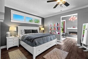 Ein Schlafzimmer mit einem Bett, Nachttischen, einem Deckenventilator, einem Kamin und einem Bücherregal.