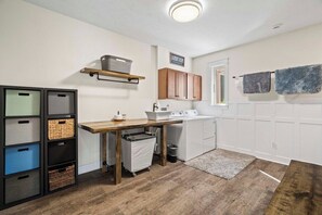 A laundry room with a washing machine, a drying rack, a shelf with baskets, and a sign indicating the room's purpose. - 6BR Farmhouse Sleeps 14 | Fire Pit + Games + Trail (Traverse City)