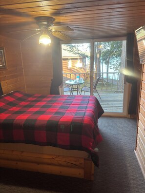 A room with a bed, a ceiling fan, and a view of an outdoor deck with a table and chairs. - Cozy 1-bedroom cabin on the Chippewa Flowage in Hayward, WI. (Hayward)