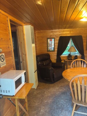 A wooden interior with a dining table, chairs, a microwave, a leather chair, and a window with curtains. - Cozy 1-bedroom cabin on the Chippewa Flowage in Hayward, WI. (Hayward)