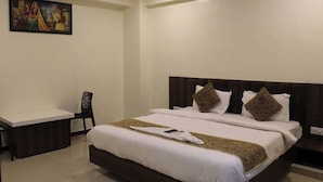 A hotel room with a large bed, a desk, and a chair. - HOTEL ROSE PALACE (Surat)