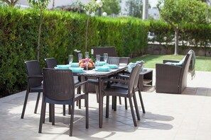 An outdoor dining area with a table set for four, surrounded by wicker chairs, and a basket of fruit on the table. - Detached villa right on the sandy beach. Alcudia (Alcúdia)