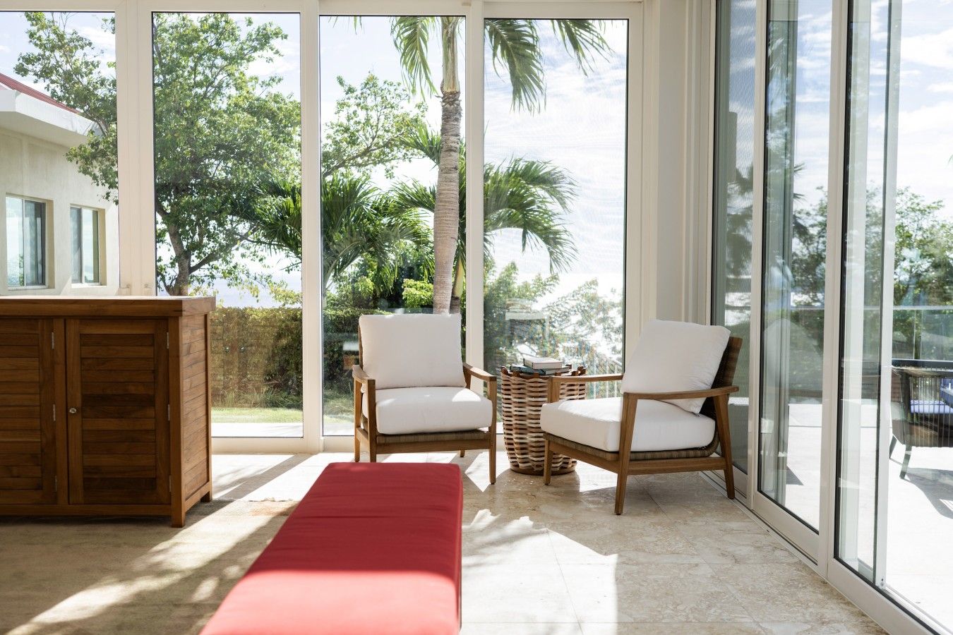 A room with a large sliding glass door, two wicker chairs, a wooden bench, and a small table with books.