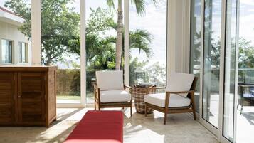 A room with a large sliding glass door, two wicker chairs, a wooden bench, and a small table with books.