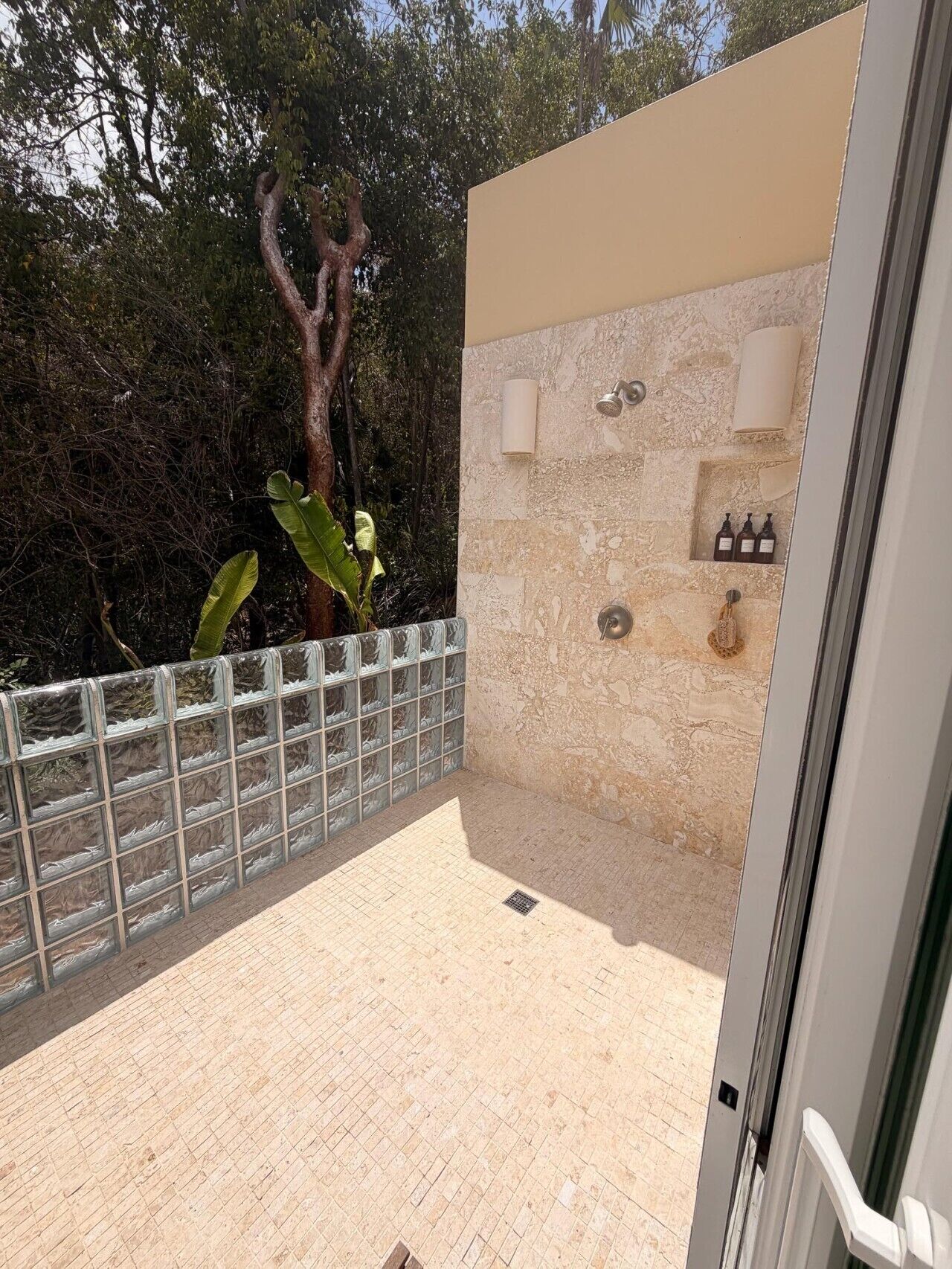 A private outdoor shower area with a stone wall, glass enclosure, and a tree in the background.
