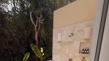 A private outdoor shower area with a stone wall, glass enclosure, and a tree in the background.