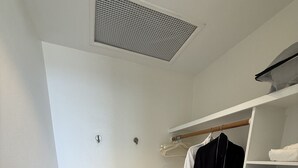 A walk-in closet with a white shelving unit, a hanging rack, and a bench.