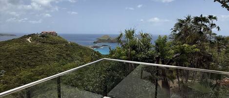 A balcony with wicker chairs overlooking a coastal landscape.
