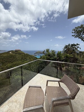 A balcony with wicker chairs overlooking a coastal landscape.