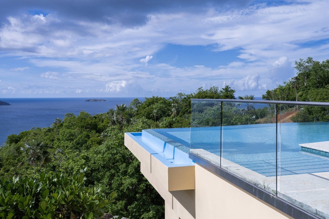 Piscina infinita moderna, com borda de vidro, com vista para uma paisagem verde exuberante e o mar.
