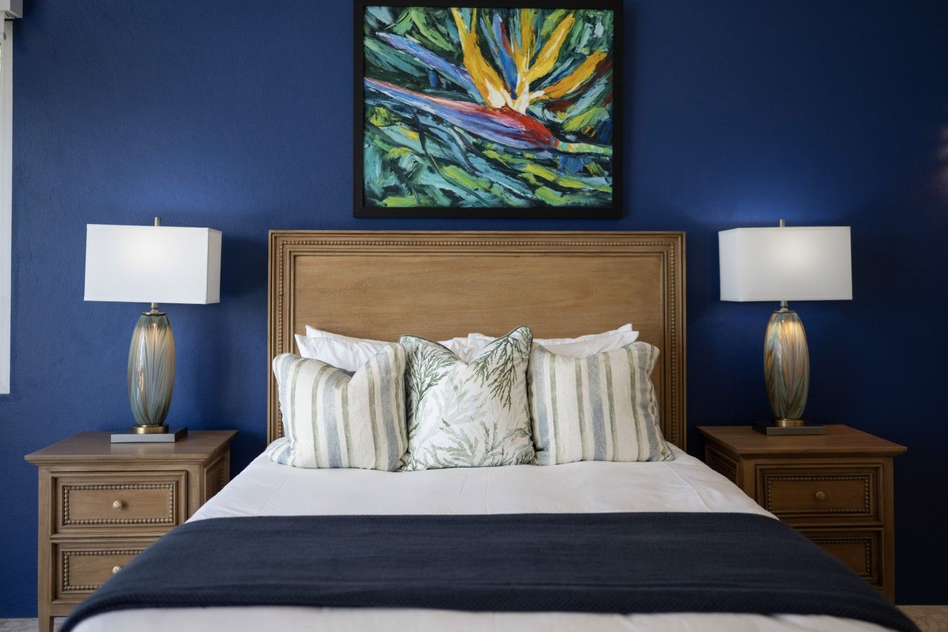 Cama com cabeceira de madeira, várias almofadas e duas luminárias de cabeceira.