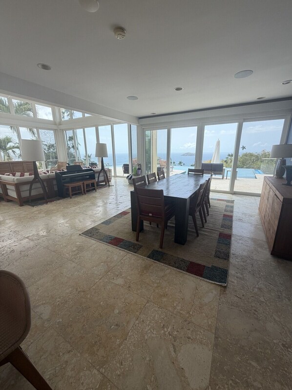 A spacious living area with a large dining table, seating, and a view of the ocean.