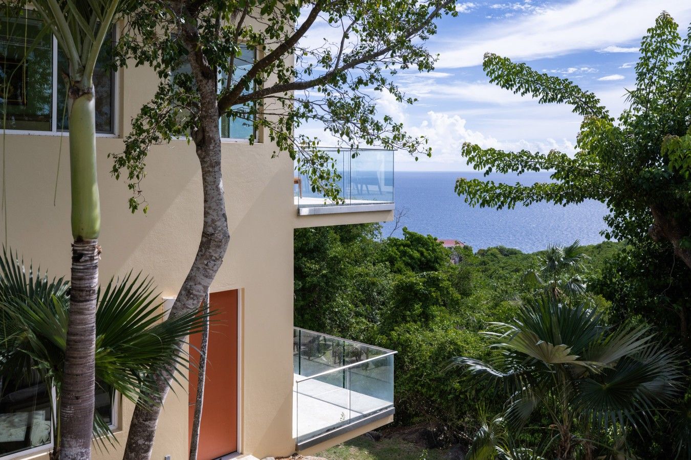 A modern building with a glass balcony overlooking a lush green landscape and a view of the sea.