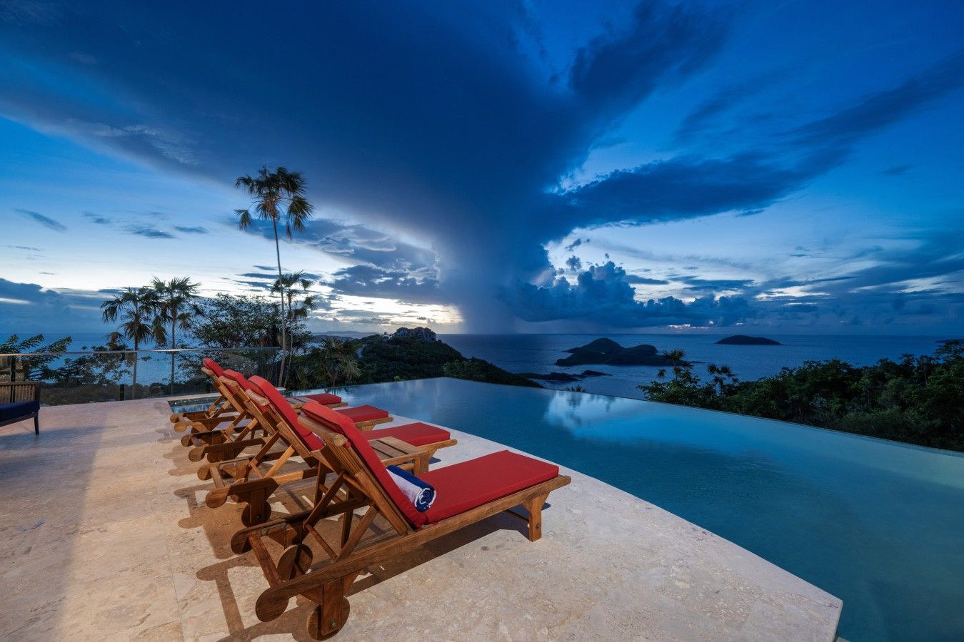 A poolside area with lounge chairs and a view of the ocean at dusk.