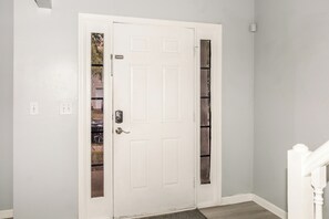 A white door with a handle and a keyhole, a doorknob, and a small window with a view of the outside.