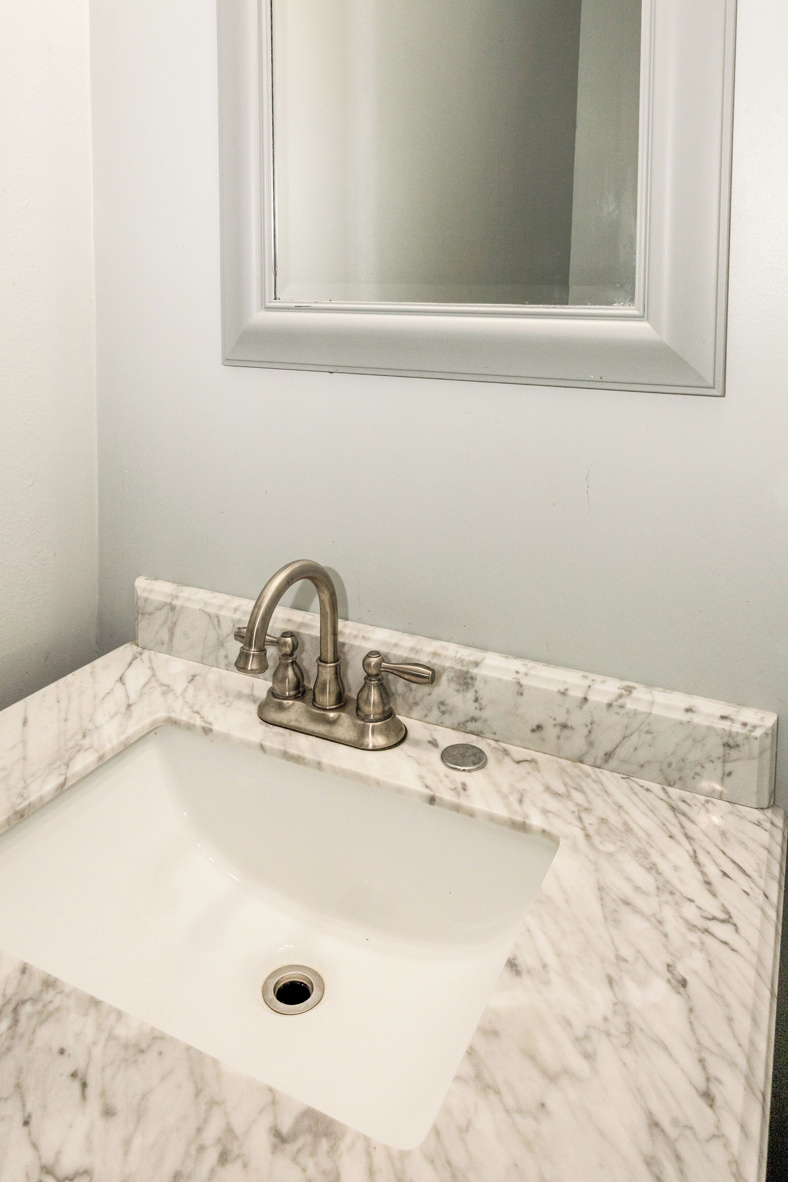 Un lavabo con un solo grifo y un espejo encima.
