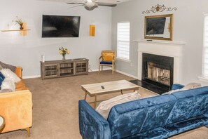 Una sala de estar con un sofá azul, una mesa de centro de madera, un televisor montado en la pared, una chimenea y un mueble pequeño.
