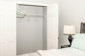 A bedroom with a bed, a bedside table with a lamp, a nightstand, and a closet with a hanging rack.