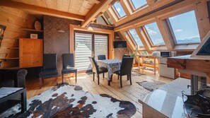 A cozy wooden interior with a dining area, a kitchen, and a large window providing a view of the mountains. - Apartamenty Sun & Snow Butorowy  (Kościelisko)