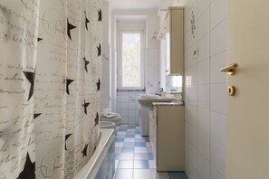 Ein schmales Badezimmer mit Schachbrettboden, einer Badewanne, einer Toilette und einem Waschbecken.