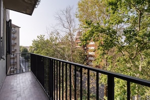Ein Balkon mit schwarzem Geländer, der auf eine Straße mit Gebäuden und Bäumen blickt.