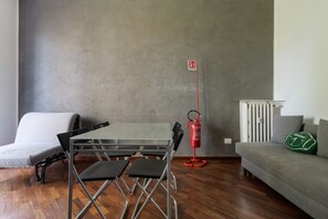 Een kamer met een opklapbare tafel, twee stoelen, een bank, een radiator en een brandblusser.