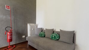 Un sofá gris con dos almohadas verdes y un extintor rojo montado en la pared.