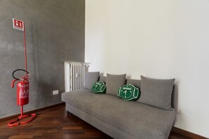 Ein graues Sofa mit zwei grünen Kissen und einem roten Feuerlöscher, der an der Wand befestigt ist.