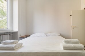Een hotelkamer met een bed, twee witte handdoeken, een raam en een deur.
