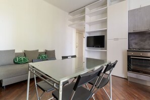 Een moderne keuken met een inbouwoven en een eethoek met een glazen tafel en stoelen.