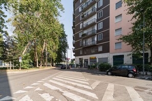 Ein mehrstöckiges Wohngebäude mit Balkonen, einer Fußgängerampel und parkenden Autos.