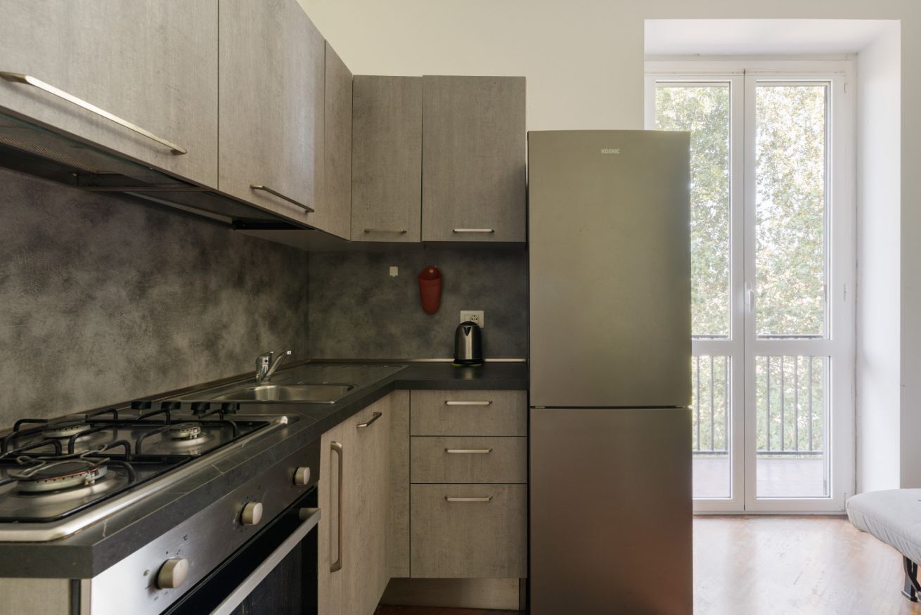 A modern kitchen with stainless steel appliances, wooden cabinets, and a large window providing natural light.