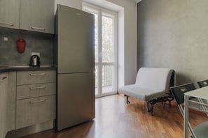 Eine kleine Küche mit Kühlschrank, Wasserkocher und Fenster mit Blick auf Bäume.