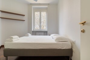 Ein Schlafzimmer mit einem Bett, zwei Regalen an der Wand, einem Fenster mit Blick und einer Tür mit Griff.