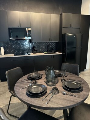 A modern kitchen with dark cabinetry, a microwave, a refrigerator, and a dining area set with plates, glasses, and cutlery. - Trendy Beach Escape w/ 2 Kings (Carolina)