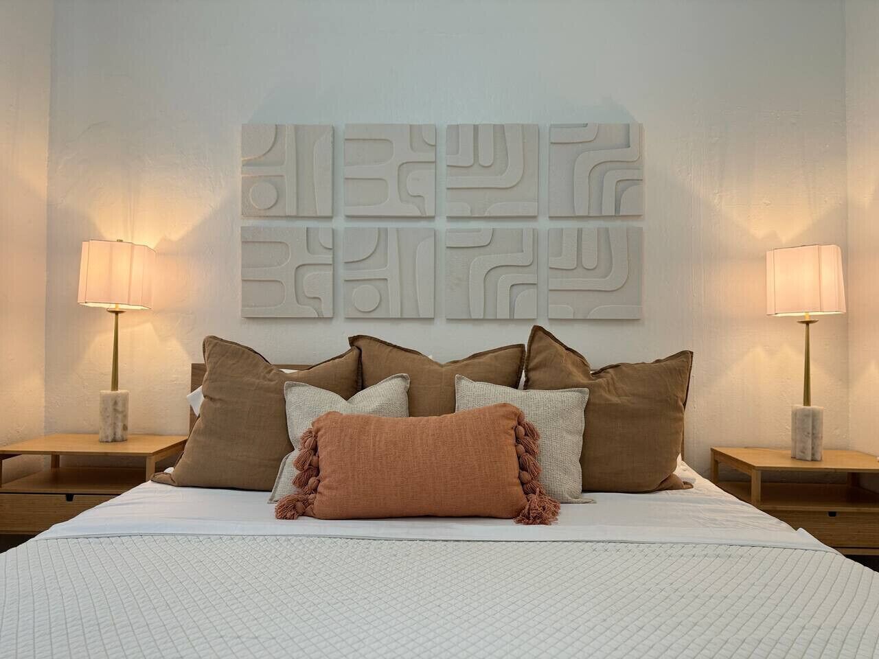 A neatly made bed with a patterned bedspread, multiple pillows, and two bedside lamps on wooden nightstands.
