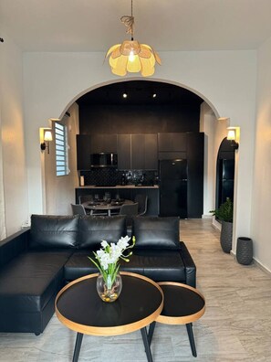 A modern living room with a sofa, two side tables, a vase with flowers, and a kitchen in the background. - Trendy Beach Escape w/ 2 Kings (Carolina)