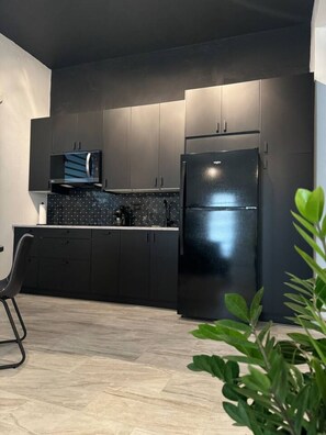 A modern kitchen with dark cabinetry, a black refrigerator, and a microwave. - Trendy Beach Escape w/ 2 Kings (Carolina)