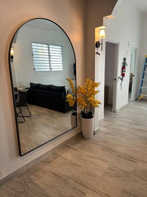 A modern interior with a large mirror, a black sofa, a potted plant, and a visible fire extinguisher. - Trendy Beach Escape w/ 2 Kings (Carolina)