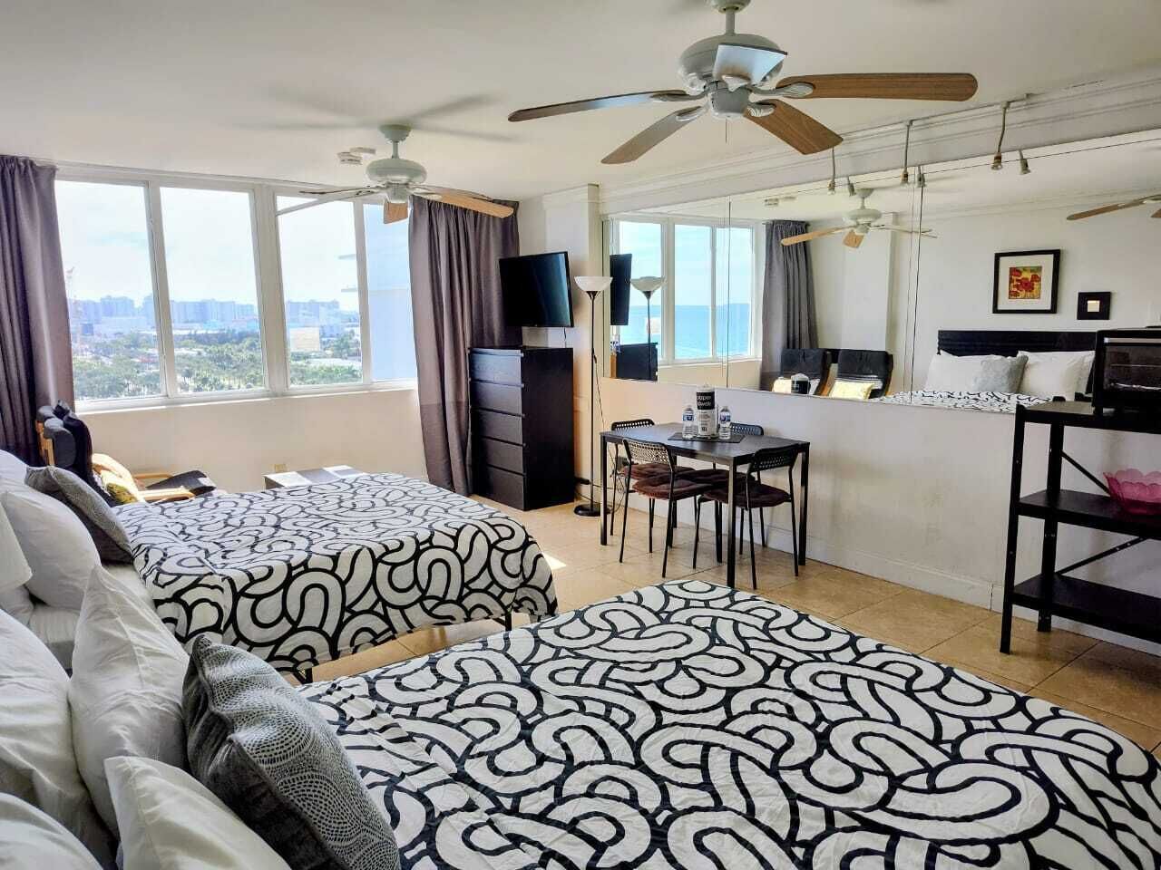 Ein Hotelzimmer mit zwei Betten, einem Esstisch, Stühlen, einem Fernseher und Blick auf die Stadt.
