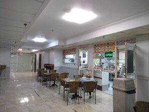 A spacious indoor area with multiple tables and chairs, a visible exit sign, and a restaurant named 'PIZZA BIANCO' with an 'OPEN' sign.